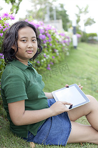 手拿平板电脑坐在绿草上的女孩