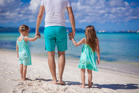 年轻父亲和他的两个小孩在海边散步的背影