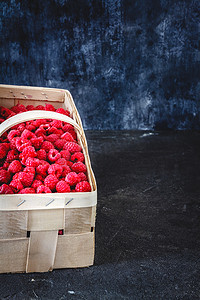 深色复古风的篮子里放着鲜亮多汁的成熟红树莓