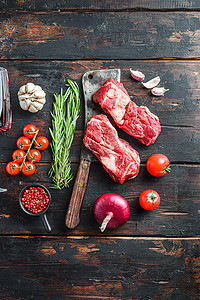 有机生夹眼牛排放在旧屠夫切肉刀上，在旧深色木桌上放上香草和调味料。