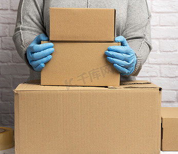 穿灰色毛衣的女人正在打包，蓝色手套拿着一堆棕色纸箱