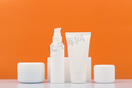 c橙色摄影照片_一套化妆品瓶放在橙色背景的白色光滑桌子上。