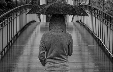 下雨天，年轻女子撑着雨伞从木桥上穿过。
