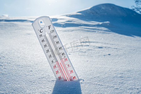 温度计在冬天躺在雪上，显示负温度。冬季恶劣气候下空气和环境温度低的气象条件。冬季结冰。阳光明媚的冬天