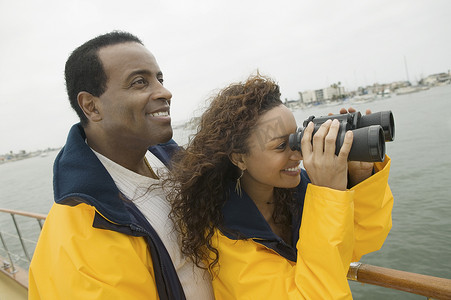 快乐的非洲裔美国女人和男人在游艇上透过双筒望远镜看