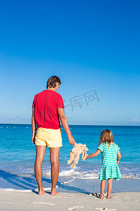 爸爸带着小女儿在加勒比海滩上拿着兔子玩具
