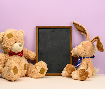 可爱的棕色泰迪熊和长耳朵的兔子坐在紫色背景的空木框之间