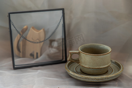 手工制作的陶瓷咖啡杯，在织物纹理桌布上饰有猫咪形状的木制玩偶。