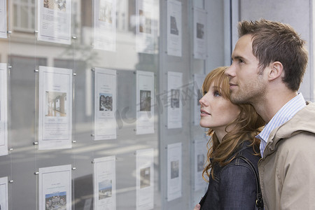 一对年轻夫妇在房地产办公室看橱窗的侧视图