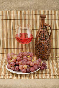 瓷瓶摄影照片_垫子上的陶瓷瓶、葡萄和酒杯
