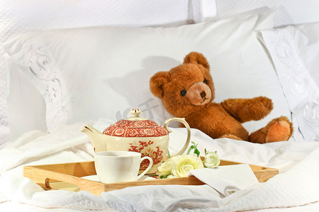 躺在床上喝茶，白色床单上放着泰迪熊