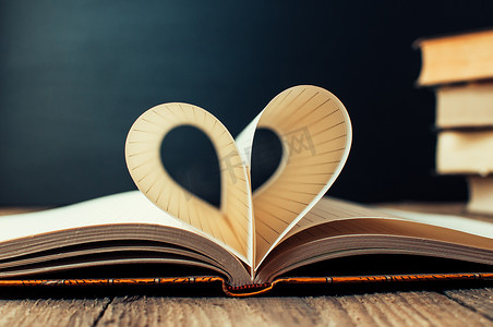 笼子里的笔记本的床单，包裹着心形。背景是一摞书和一块黑板。教育理念。情人节。复制空间。质朴和复古。概念爱。