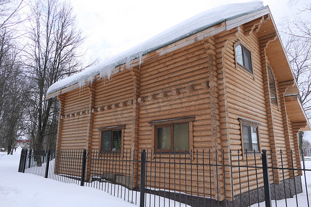 冬天，篱笆后面的一座大木屋顶着雪，屋顶上挂着冰柱。