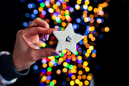 发光装饰星星摄影照片_持有圣诞闪闪发光的星星装饰孤立在背景与模糊的灯光。