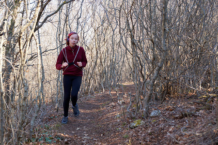 戴耳机的少女背着背包沿着森林小径奔跑
