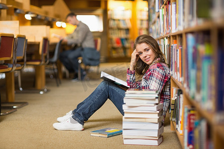 在图书馆地板上的俏丽的微笑的学生阅读书