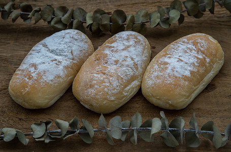 撒花矢量卡通摄影照片_三个自制的甜奶油软面包，在古老的乡村木桌上撒上糖霜。