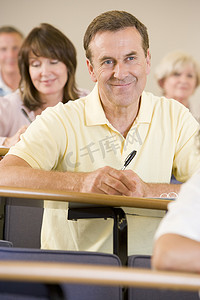 男子坐在成人教室里，背景是学生（选择性焦点）