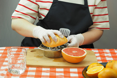 一名年轻女子在手工榨汁机上用橙子和葡萄柚鲜榨果汁。