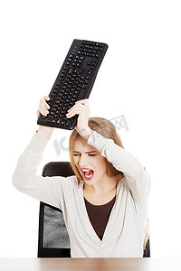 疯狂工作摄影照片_桌子后面的美丽休闲女人试图打破键盘