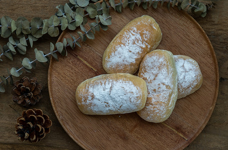 四个自制的甜奶油软面包，在质朴的木桌上的圆形木板上撒上糖霜。