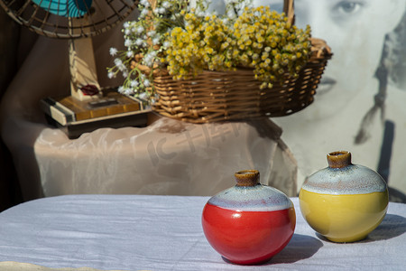 圆扇子摄影照片_白色纹理桌布上的两个小陶瓷花瓶，前面是编织篮子里的花束和复古扇子。