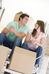 楼梯上搬箱子摄影照片_一对夫妇坐在楼梯上，带着箱子在新家微笑