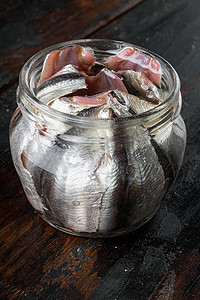 凤尾鱼鱼罐头装在锡罐海鲜里，装在玻璃罐里，放在旧的深色木桌背景上。