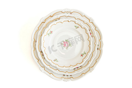 堆叠的三个白色餐盘和碟子，上面有鲜花和波浪形边缘的顶视图，被隔离