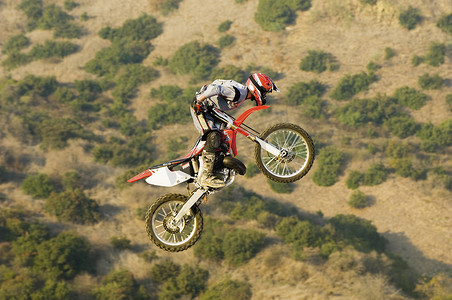 全长男性摩托车骑手骑着摩托车在空中飞翔，背景是山