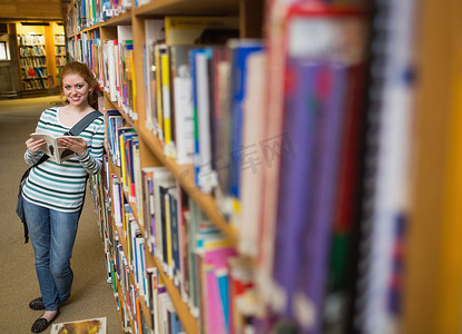 读书成长手册摄影照片_图书馆书架上倾斜的快乐学生阅读书