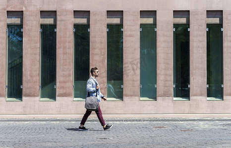 单包摄影照片_一个时髦的年轻人拿着单肩包走路的肖像