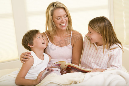 有两个小孩的女人坐在床上看书微笑