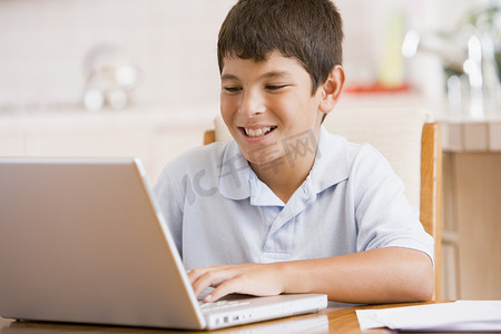 厨房里的小男孩带着笔记本电脑和文书工作微笑