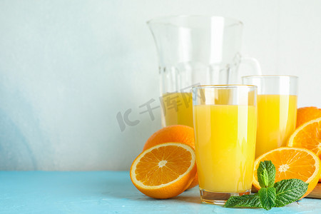 与玻璃器皿中的新鲜橙汁、薄荷和木制榨汁机在白色背景的彩色桌子上组成，文本空间。