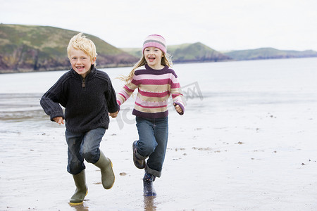 小孩在沙滩玩耍摄影照片_两个在沙滩上奔跑的小孩手牵着手微笑