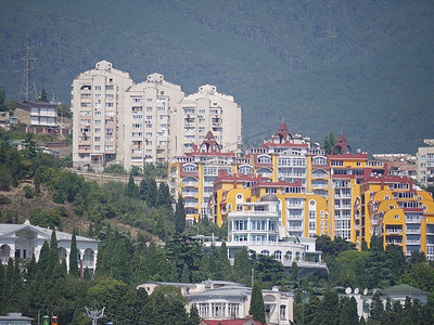 高大的现代住宅、私人别墅和酒店位于森林覆盖的山坡上的绿树之间。