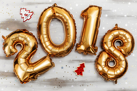 明亮的金属金色气球代表 2018 年、圣诞节、新年气球，白色木桌背景上闪闪发光的星星