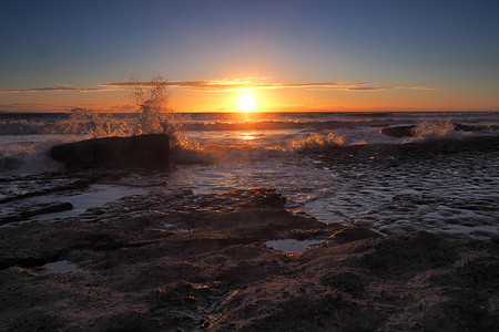 泳池晚上摄影照片_日落时云层和海浪拍打着岩石，南威尔士邓拉文湾