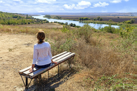 在一个阳光明媚的秋日，一位年轻女子坐在木凳上看着平静的南布格河。