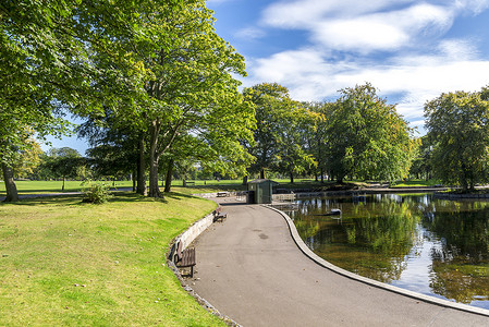 苏格兰阿伯丁 Duthie 公园的一个小浅池周围有长椅的风景优美的小径