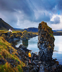 岩石海滩上的游客看着冰岛 Arnarstapi 的一栋小房子