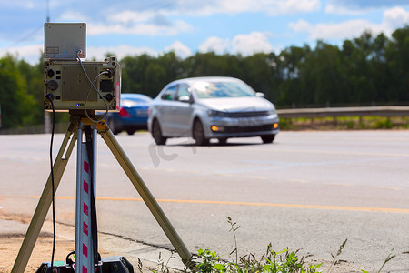 在夏日白天道路上工作的移动速度摄像装置，背景中有模糊的白色汽车