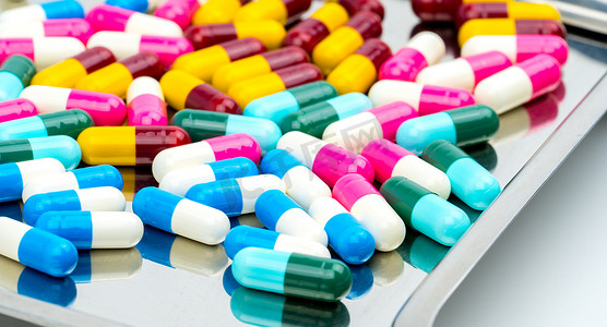 五颜六色的抗生素胶囊药片在不锈钢药盘上有阴影，抗菌药物耐药性概念。