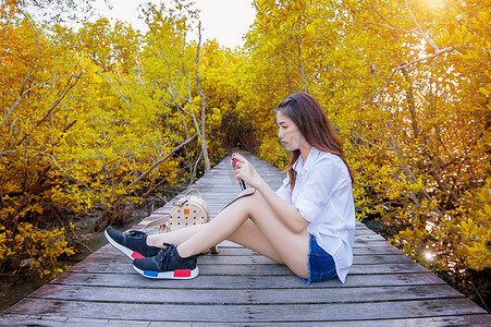 秋天，女孩独自坐在木桥上，手拿着相机。