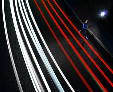 年轻的运动员在夜路上奔跑，有汽车灯迹。
