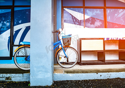 木杆子摄影照片_自行车靠在木鞋架附近的一根杆子上，木鞋架放在一栋带耀斑灯的建筑物的水泥地板上。