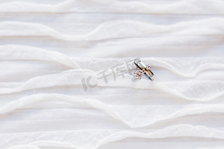 带钻石的金色结婚戒指位于白色织物上。