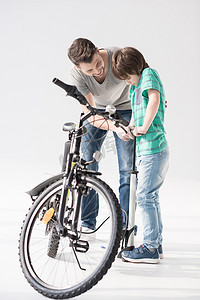 儿子给父亲摄影照片_快乐的父亲教儿子用白色给自行车轮胎打气