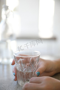 玻璃杯里的水，女人的手和咖啡店桌子上的瓶子